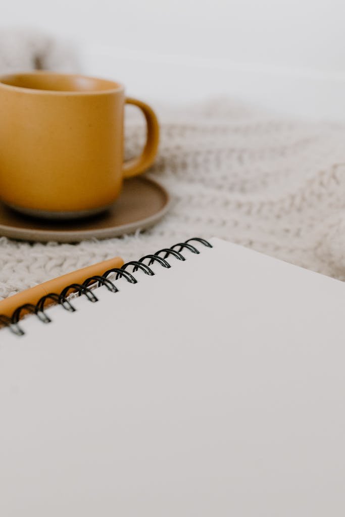 A warm coffee cup next to a blank notebook on a knitted blanket, perfect for cozy mornings.
